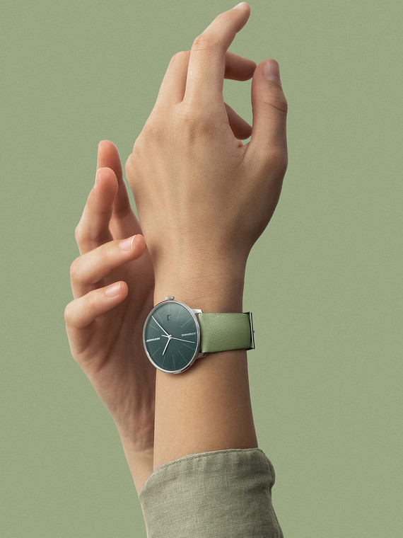 The JUNGHANS Meister Fein Automatic Moss Green And Green Apple Ref# 27/4357.00 is a watch with a moss green dial and a green leather strap. It has a 39.5 mm x 10.3 mm stainless steel case with a domed sapphire crystal that has an anti-reflective coating on both sides. The watch has a minimalistic appearance with a circular case that has thin and elongated indices, hour, minutes, and seconds hands. The domed sunburst dial shimmers in different shades depending on the angle of the light, and the 12 o'clock index has eight diamonds. The 12 o'clock index is visually balanced by the vertical logo at 6 o'clock.